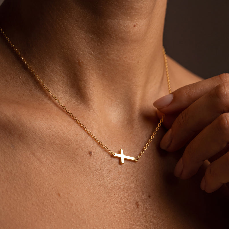 Dainty gold sideways cross necklace on a fine stainless steel chain