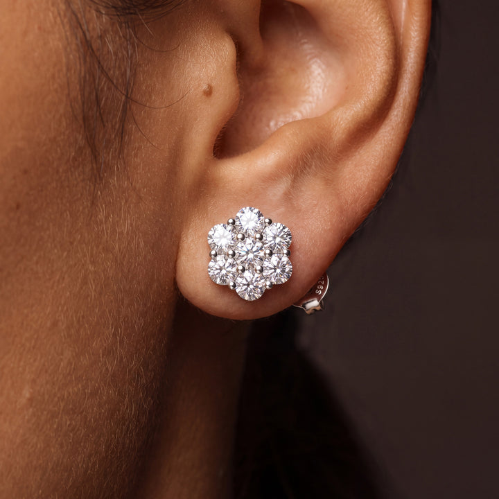 Moissanite flower cluster stud earring worn on an ear, seven round stones in a rhodium-plated silver setting